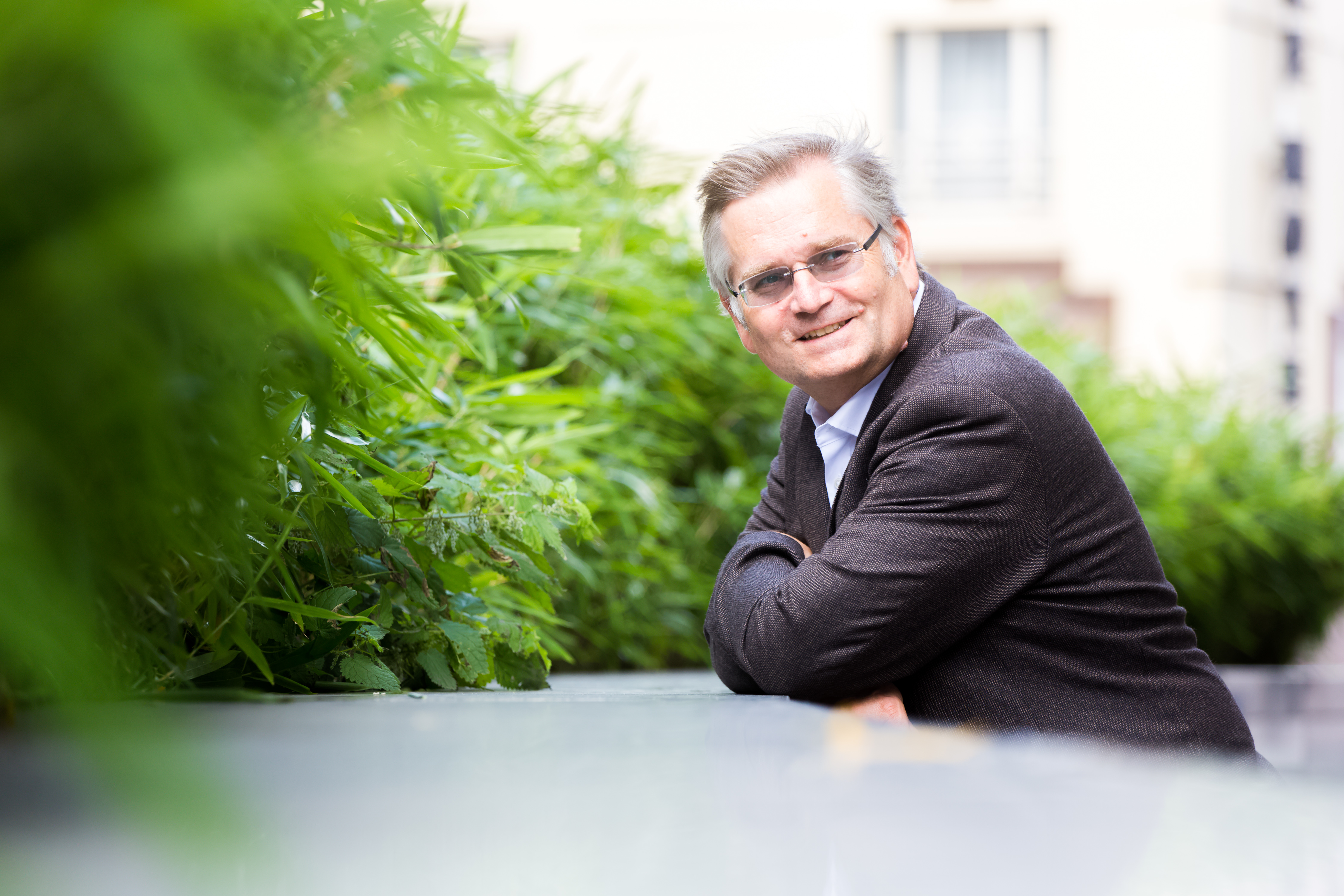 Man in suit and glasses smiling at the camera in a garden. 