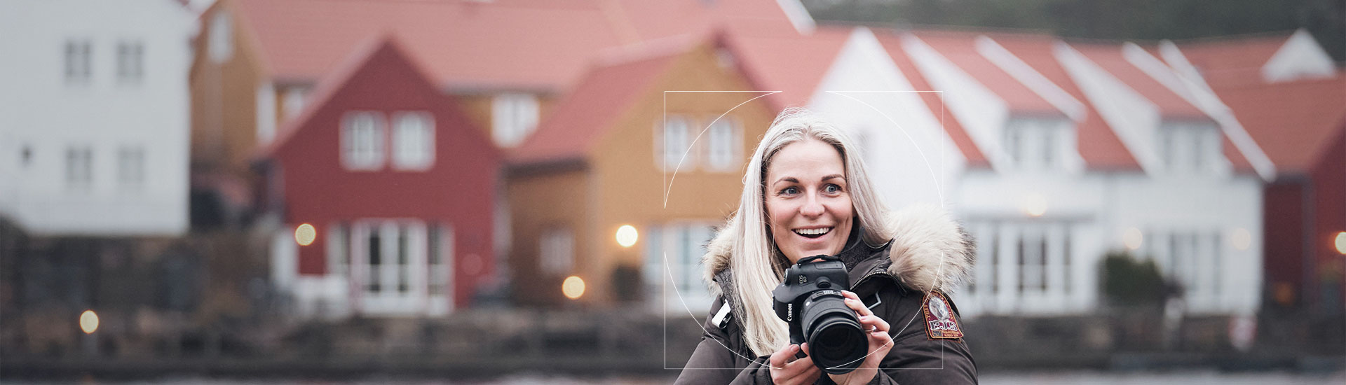 Woman in brown winter coat holding a black camera and smiling 