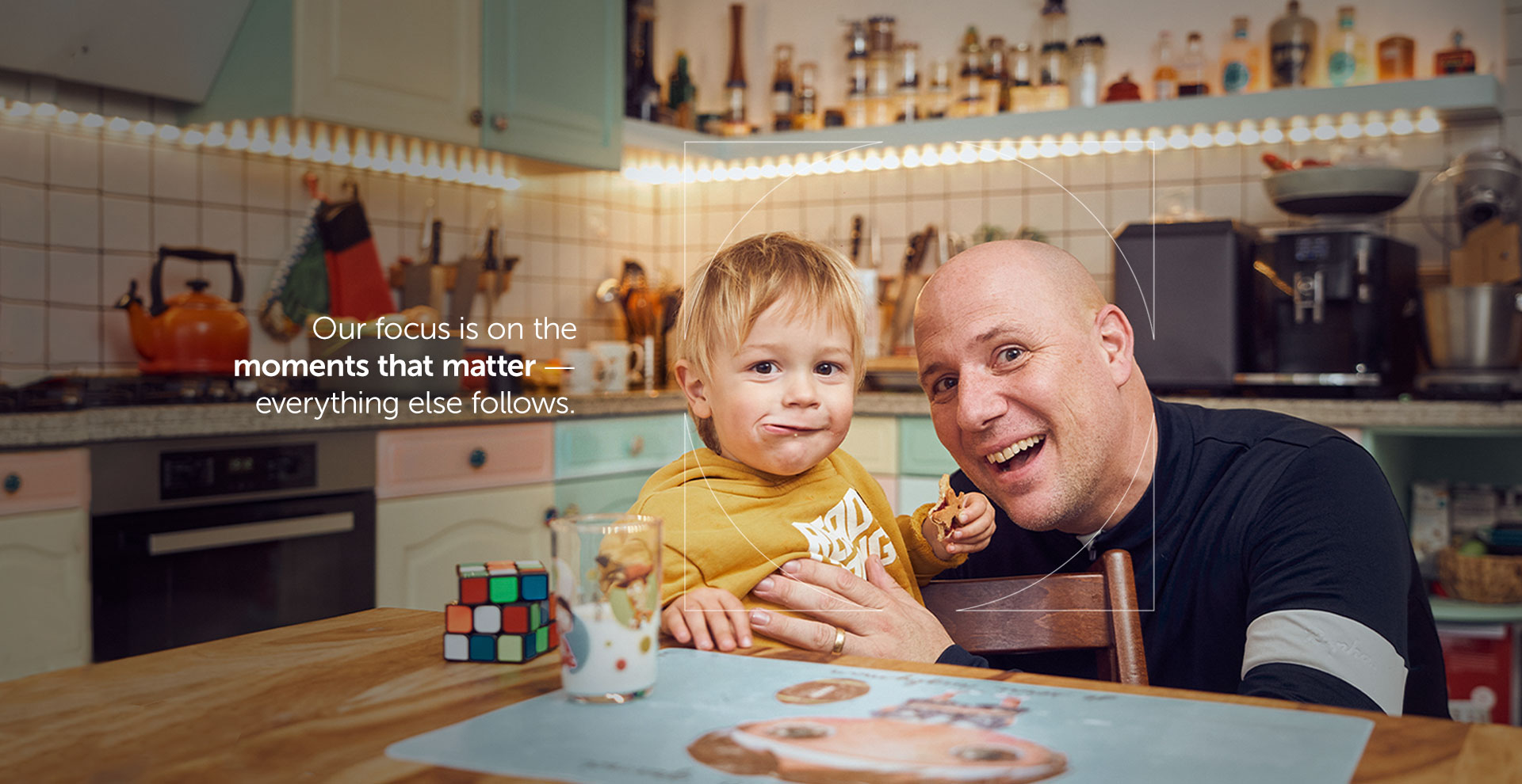 Father holding child while smiling in a kitchen with overlaying text on UCB's focus on the moments that matter