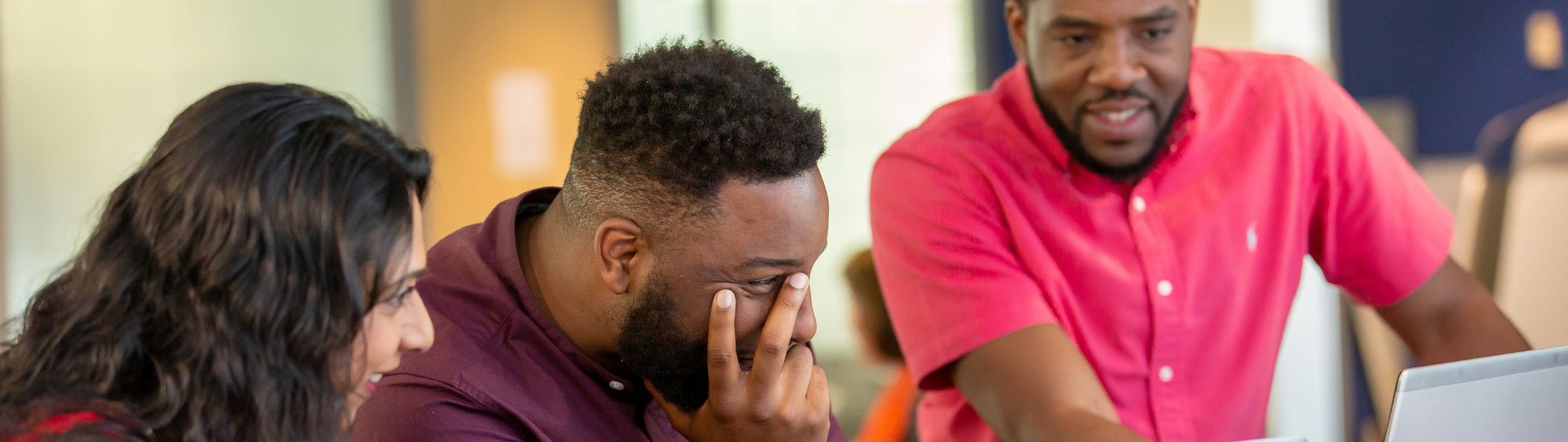 Three UCB employees in colored shirts smiling and looking at a computer screen together