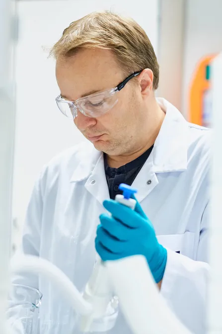 Scientist in white lab coat and blue gloves holds research tool